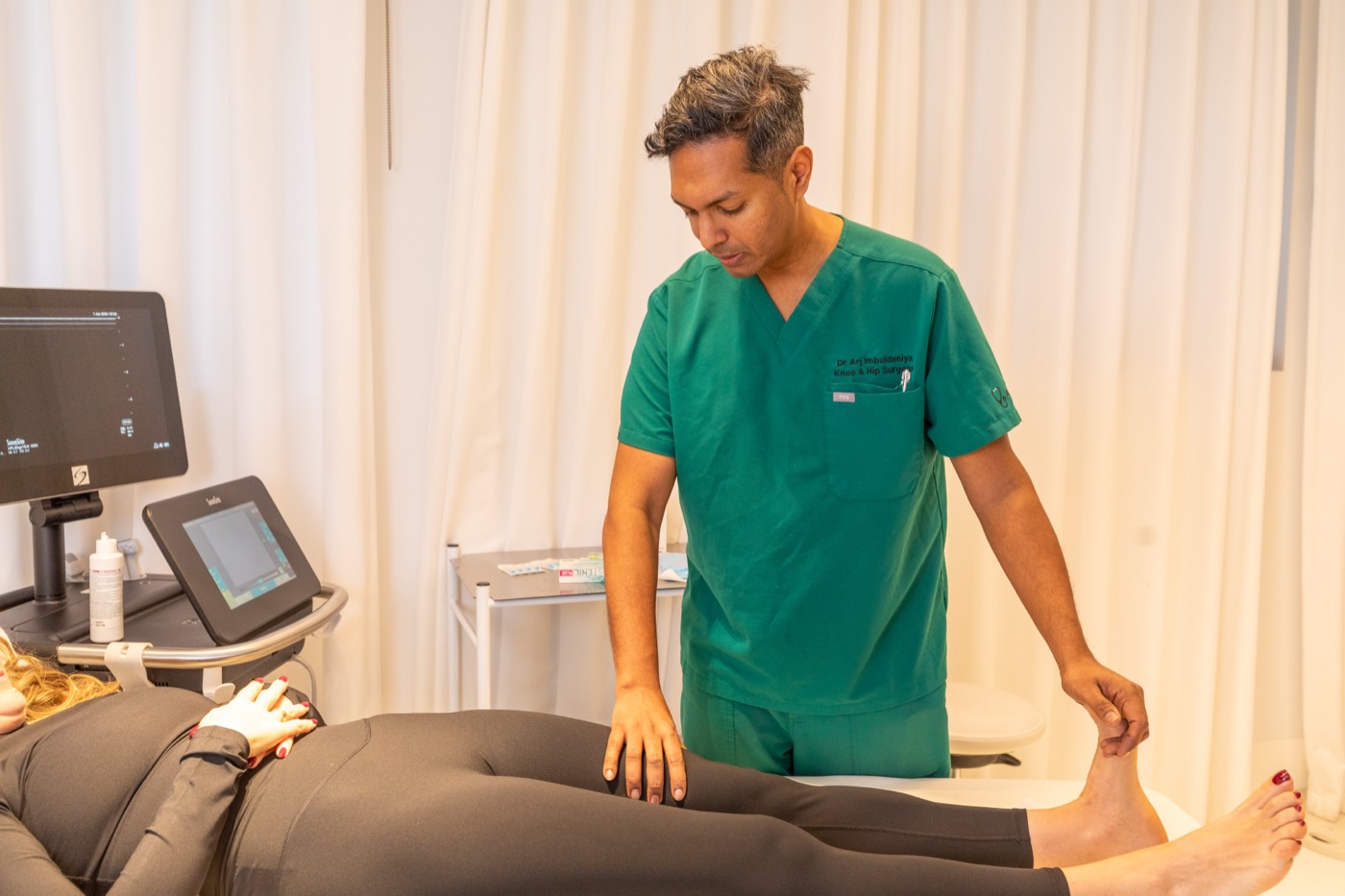 Dr Arj Imbuldeniya examining a patient's knee during a consultation